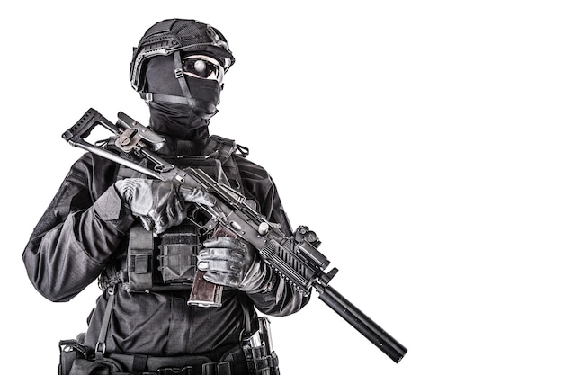 Retrato de estúdio de um membro das forças especiais da polícia, atirador do grupo de reação rápida em uniformes pretos, capacete, escondido atrás de máscara e óculos, armado com rifle de assalto isolado no branco, copyspace
