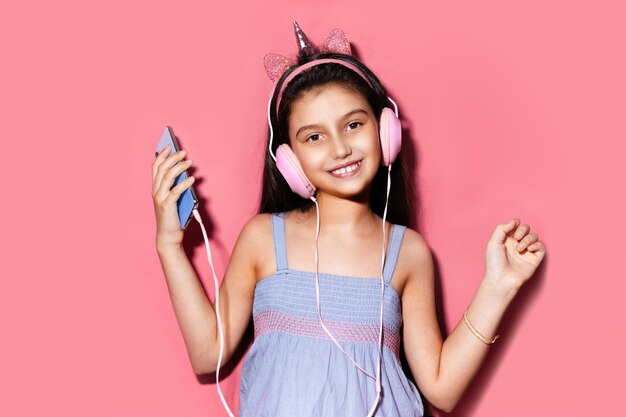 Retrato de estúdio de uma criança feliz, segurando o smartphone nas mãos e usando fones de ouvido