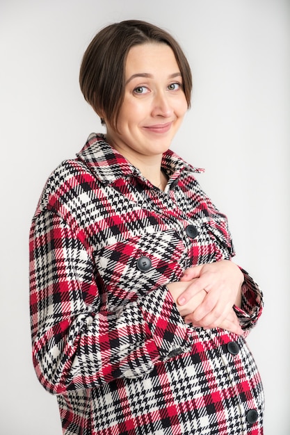 Retrato de estúdio de uma jovem adulta com roupas quentes para casa, conceito de gravidez feliz, parede branca