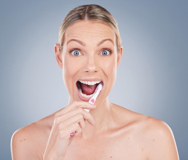 Retrato de estúdio de uma jovem atraente escovando os dentes contra um fundo cinza