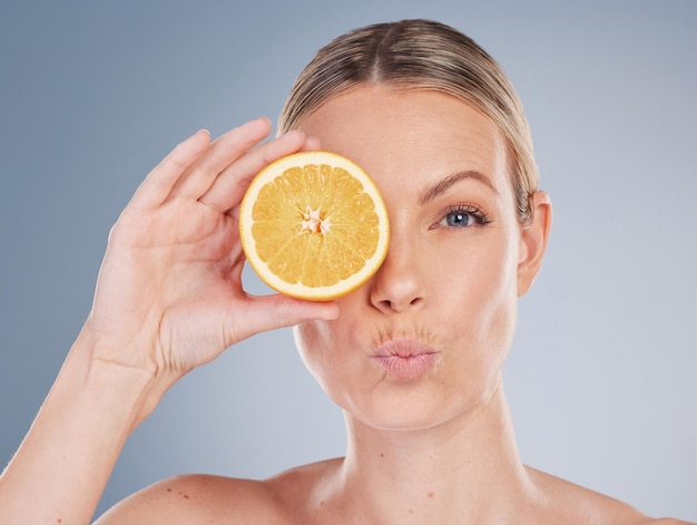 Retrato de estúdio de uma jovem atraente posando com meia laranja contra um fundo cinza