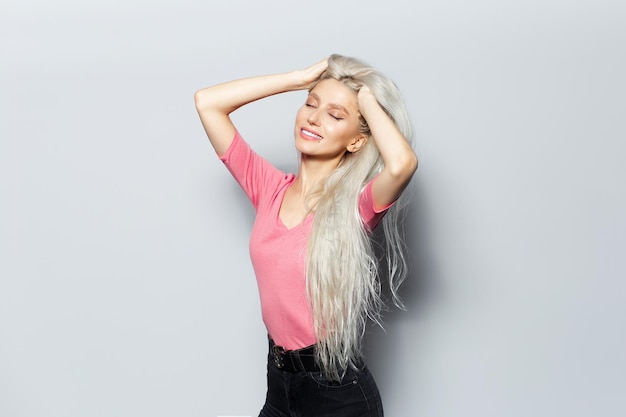 Retrato de estúdio de uma jovem bonita feliz com as mãos na cabeça sobre fundo branco vestindo camisa rosa