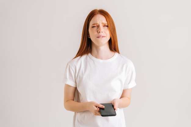 Retrato de estúdio de uma jovem desapontada lendo mensagem online usando telefone celular em branco