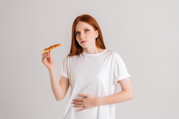 Retrato de estúdio de uma jovem descontente sentindo dor no estômago depois de comer pizza sofrendo