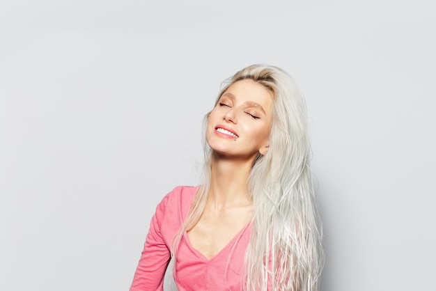 Retrato de estúdio de uma jovem muito sorridente com cabelo loiro na camisa rosa sobre fundo branco