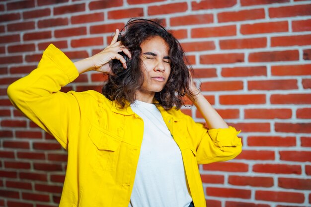 Retrato de estúdio de uma jovem rabugenta vestindo um suéter amarelo e com fones de ouvido na cabeça