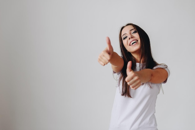 Retrato de estúdio de uma jovem sorridente, mostrando o polegar para cima em um fundo branco isolado