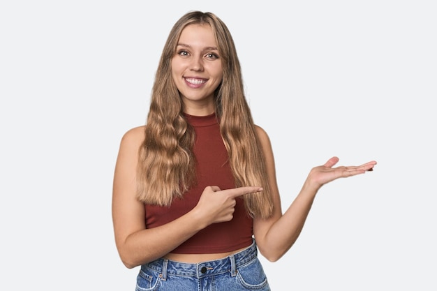 Foto retrato de estúdio de uma mulher loira caucasiana excitada segurando um espaço de cópia na palma da mão