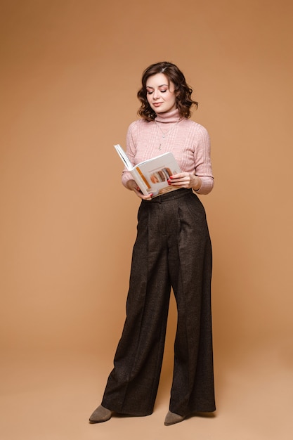 Retrato de estúdio de uma mulher morena elegante em roupas casuais, segurando um livro aberto nas mãos e lendo. Foto stock de comprimento total isolar no fundo.