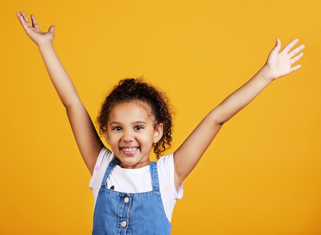 Retrato de estúdio e criança animada com as mãos para cima e sorriso no rosto em fundo amarelo Garotinha com felicidade despreocupada e atitude positiva ou celebração feliz ou anúncio surpresa