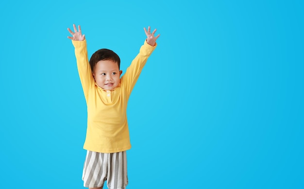 Retrato de expressão sorridente de menino asiático levanta as mãos e olhando ao lado isolado em fundo azul com espaço de cópia