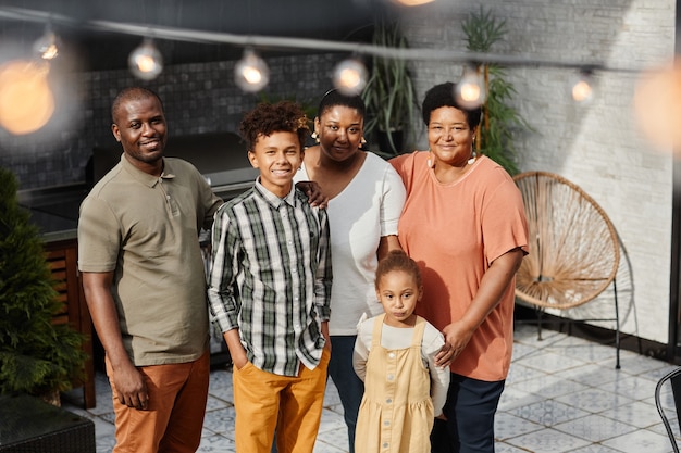 Retrato de família afro-americana feliz olhando para a câmera enquanto posava no terraço ao ar livre multigen ...