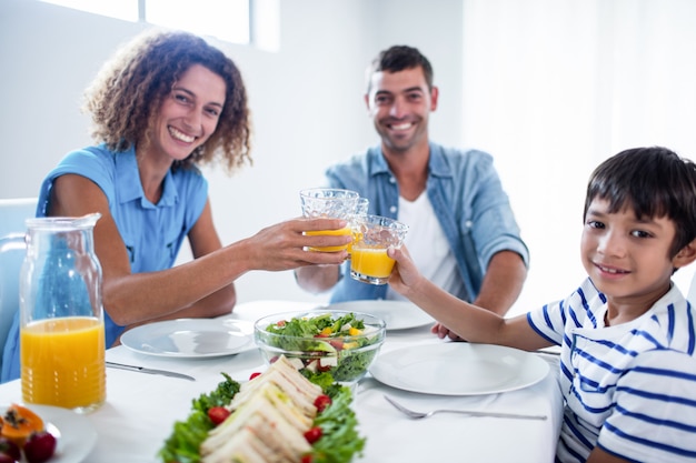 Foto retrato de família brindando copos de suco de laranja enquanto tomando café da manhã