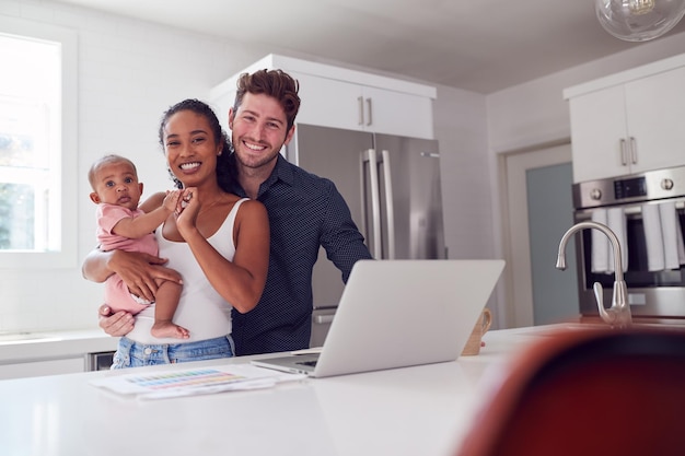 Retrato de família com filha bebê na cozinha usando laptop no balcão