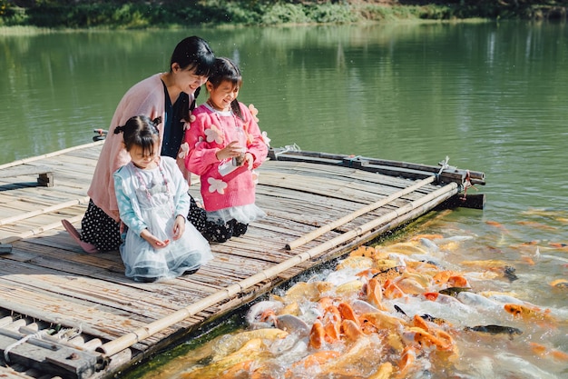 Retrato de família de mãe e filhos alimentando peixes no lago