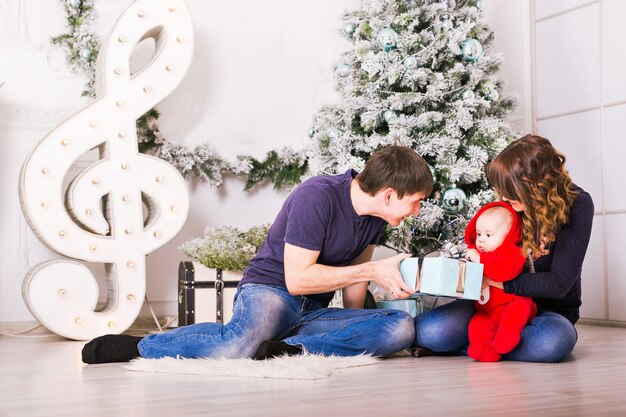 Retrato de família de Natal na sala de estar de férias em casa, brincadeiras de cachorro e crianças, caixa de presente para presente, decoração da casa por velas de árvore de Natal Garland