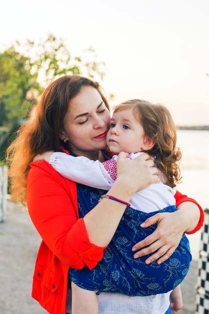 Retrato de família envolvendo uma menina criança em um estilingue azul e abraços de mãe