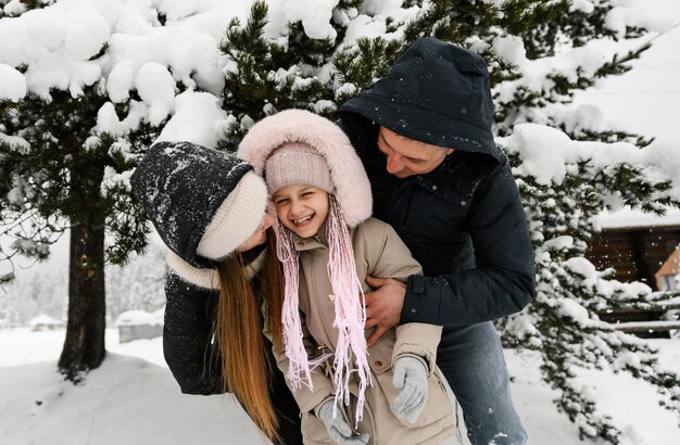 Retrato de família feliz brincalhão na floresta de inverno. Mãe, pai e filha brincando com neve. Gostando de passar um tempo juntos. Conceito de familia