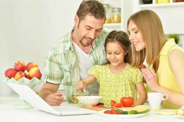 retrato de família feliz cozinhando na cozinha com laptop