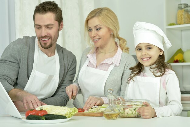 Retrato de família feliz cozinhando na cozinha com laptop