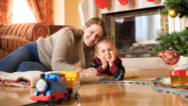 Retrato de família feliz e sorridente, deitada no chão e olhando para o trem andando na ferrovia sob a árvore de Natal na sala de estar