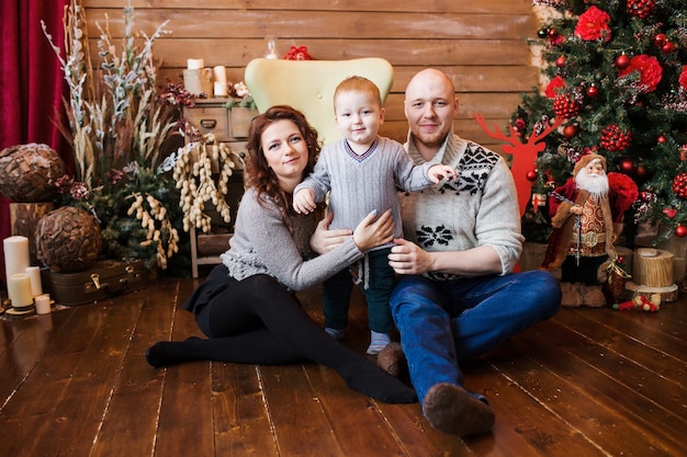 Retrato de família feliz no Natal, mãe, pai e filho sentados na cadeira alta em casa, decoração de natal e presentes em torno deles