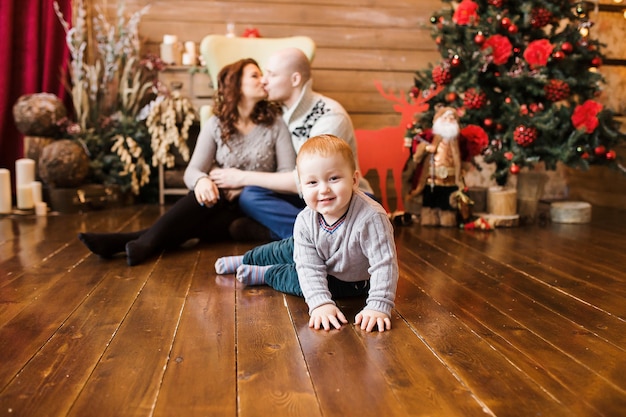 Retrato de família feliz no natal, mãe, pai e filho sentados na cadeira alta em casa, decoração de natal e presentes em torno deles