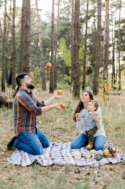 Retrato de família feliz sentado em uma manta quadriculada com frutas na floresta de outono