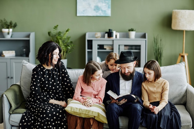 Retrato de família judia com três filhos lendo livro juntos em ambiente doméstico moderno