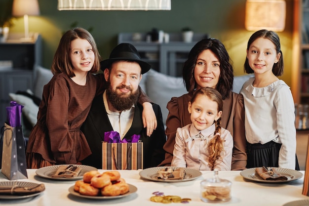 Retrato de família judia ortodoxa olhando para a câmera enquanto está sentado à mesa de jantar em casa aconchegante