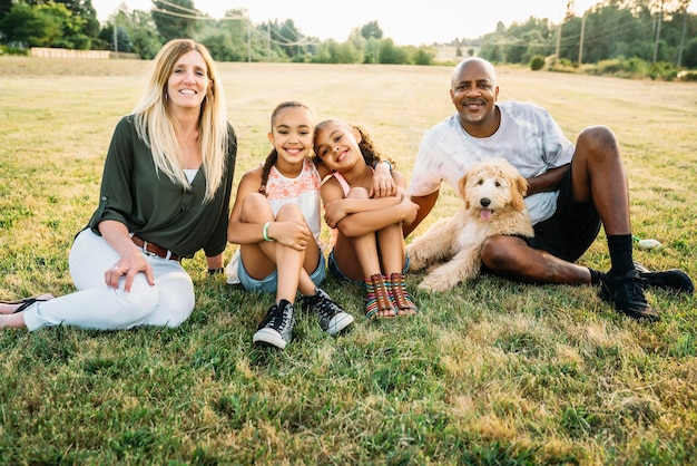 Retrato de família mestiça em campo com filhote de labradoodle