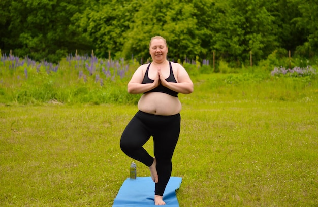 Retrato de felicidade plus size mulher praticando ioga ao ar livre