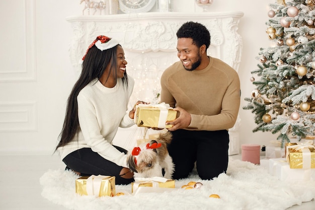 Retrato de feliz casal negro segurando presentes e sentado perto da árvore de Natal