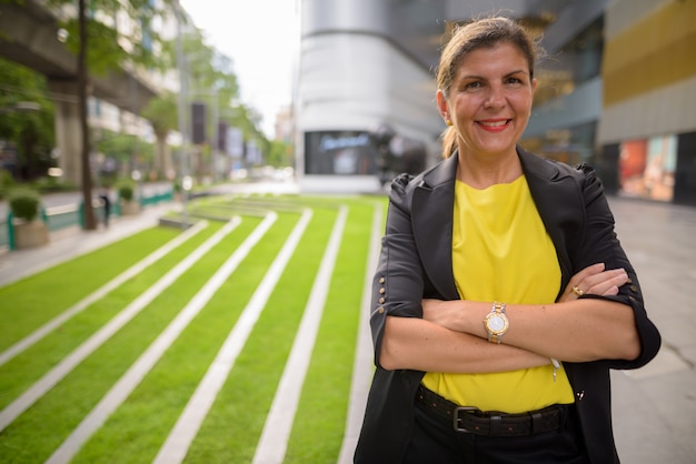 Retrato de feliz empresária madura ao ar livre com os braços cruzados