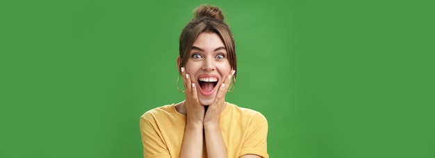 Foto retrato de feliz, encantada e surpreendida jovem feminina de camisa amarela apertando as mãos para