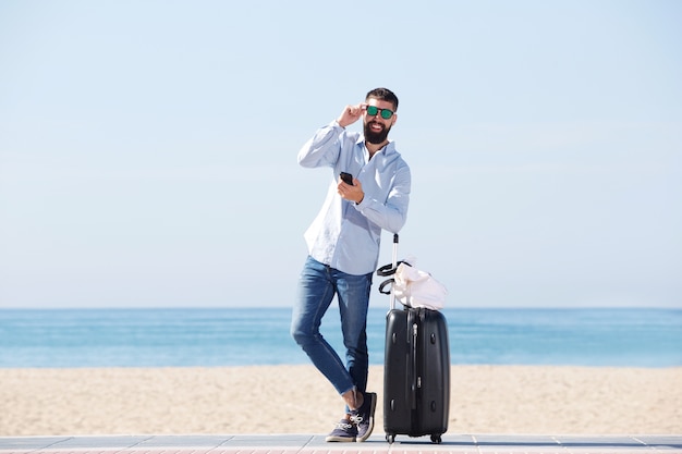 Retrato, de, feliz, homem, com, mala, e, telefone móvel, ficar, ligado, praia