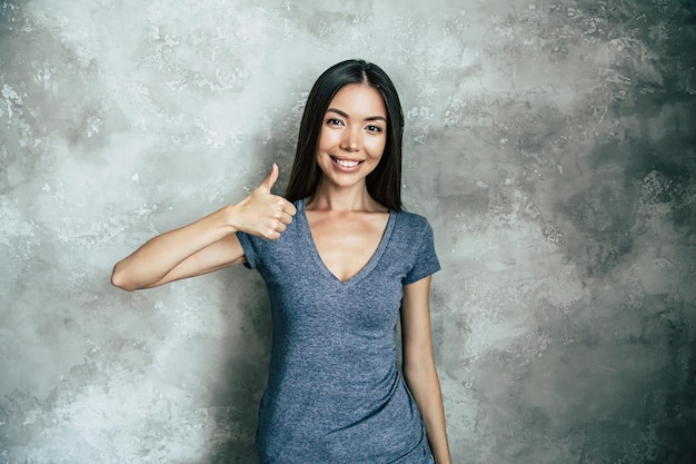 Retrato de feliz linda jovem asiática em t-shirt sobre parede de concreto