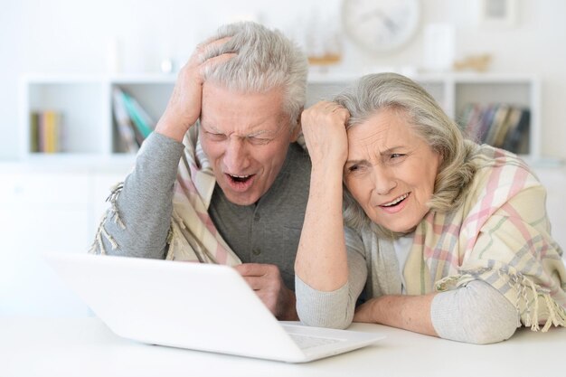 Retrato de feliz lindo casal sênior com cobertor usando laptop em casa