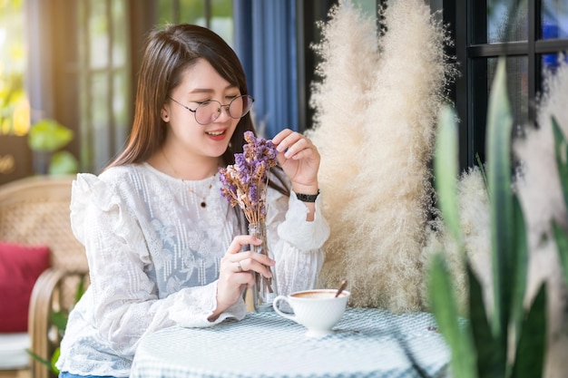 Retrato de feliz Mulher atraente asiática cheirando flores roxas Buquê de lavanda com xícara de café parecia relaxar em uma cafeteria como pano de fundo