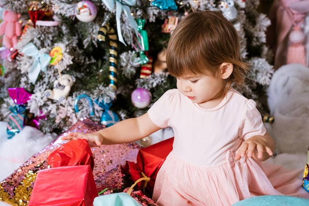 Retrato de feliz Natal feliz feriados de ano novo da menina de vestido rosa senta-se no chão com pil ...