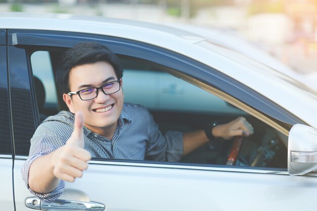 Retrato de feliz sorridente jovem asiático viajante na estrada mostrando os polegares enquanto dirige seu carro.