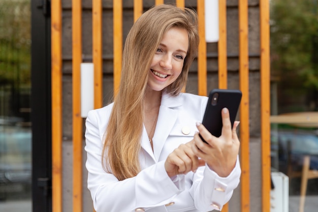 Retrato de feliz sorridente jovem empresária com cabelos longos, usando um smartphone