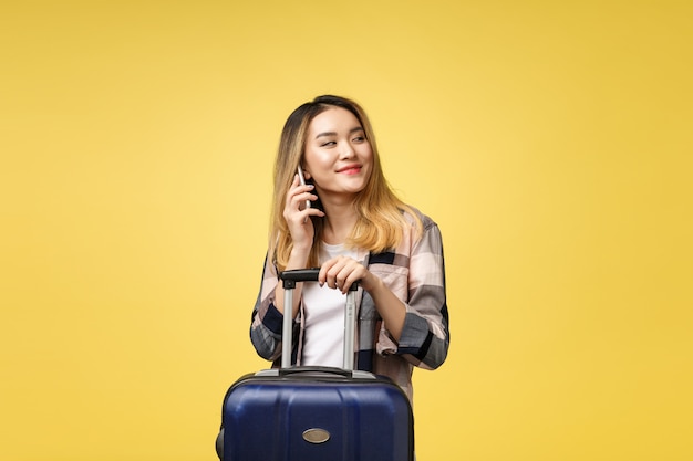 Retrato de feliz viajante feminino asiático com mala e olhando para celular