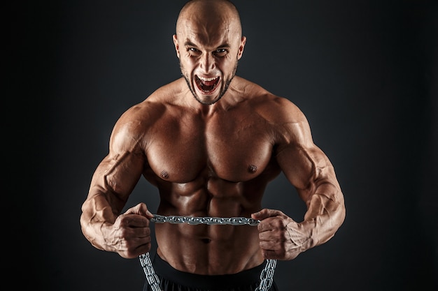 Retrato de fisiculturista agressivo tentando rasgar a corrente de metal