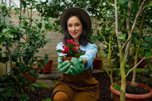 Retrato de florista atraente jovem mostrando belo vaso de flores para a câmera. Conceito de trabalho de estufa de jardim