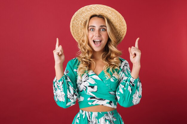 Retrato de fofura chocada gritando jovem linda loira linda mulher em vestido posando isolado sobre a parede vermelha apontando