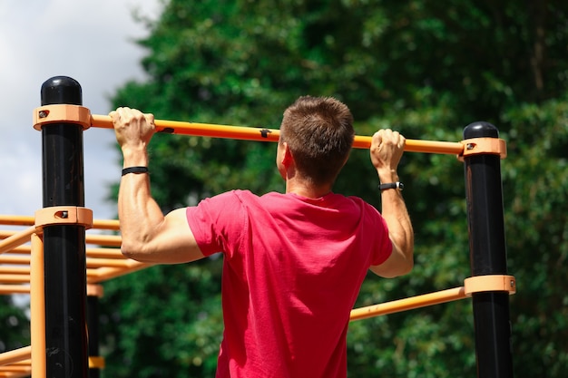 Retrato de forte desportista, fazendo exercícios de força. Atleta puxando para cima na barra horizontal