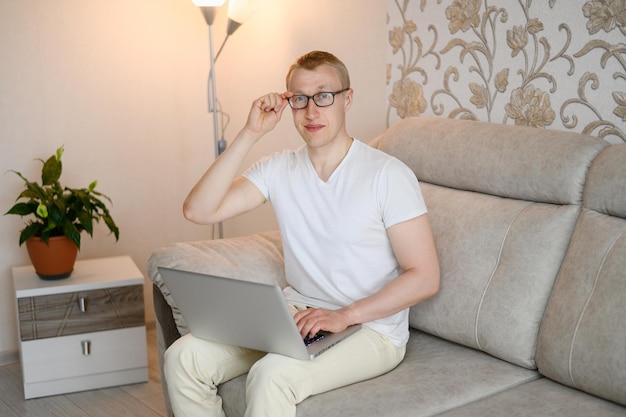 Retrato de freelancer ajustando óculos sentado no sofá com laptop em casa