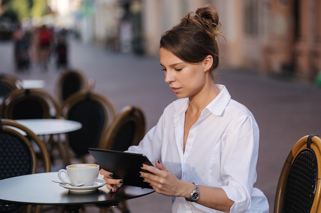 Retrato de freelancer feminino atraente usando tablet no café no terraço