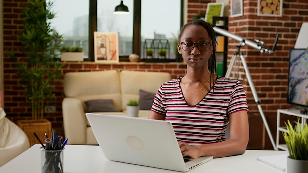 Retrato de freelancer feminino trabalhando remotamente em casa, usando laptop e conexão online para fazer trabalho de negócios na sala de estar. Empregado de escritório fazendo trabalho remoto de inicialização na mesa.
